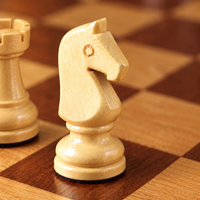 Gros plan sur un cavalier d’échecs en bois clair posé sur un échiquier en bois, avec une autre pièce.