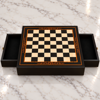 Échiquier en bois avec cadre noir, damier clair et noir bordé d’un liseré cuivré et décoré d’arabesques, posé sur une surface en marbre blanc avec ses deux tiroirs ouverts.