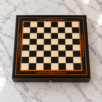 Petit échiquier en bois de 24 cm, avec cadre noir, damier clair et noir, liseré cuivré et arabesques décoratives cuivrées, présenté sur une table en marbre blanc.