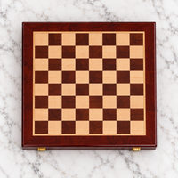 Échiquier en bois de voyage pliable, présenté ouvert sur une surface en marbre blanc, avec un damier en bois clair et brun foncé.