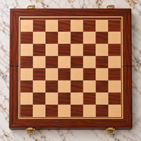 Vue de dessus d’un échiquier pliable en acajou de 45 × 45 cm, vide de toute pièce, avec un damier composé de cases claires et de cases en acajou veinées, un cadre en bois travaillé et quatre fermoirs dorés, posé sur une table en marbre blanc veiné
